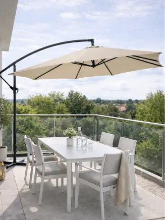 Moderner Balkon mit beigem Ampelschirm &uuml;ber weisser Sitzgruppe und Blick ins Gr&uuml;ne